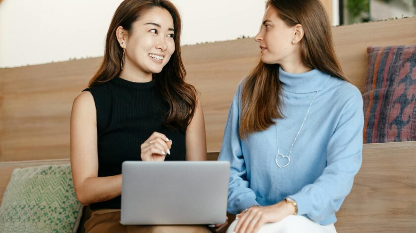 Two diverse women having a cheerful business discussion using a laptop indoors.