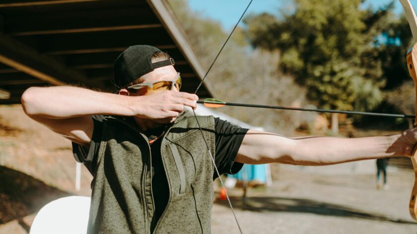 A man aiming a bow and arrow in an outdoor archery range, focusing on the target.