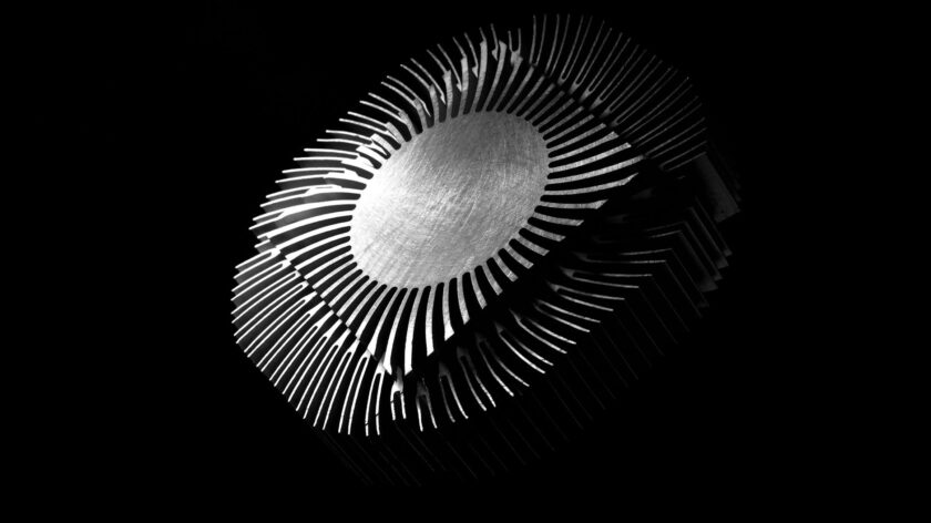 Close-up abstract image of a metallic heat sink with intricate patterns on a black background.