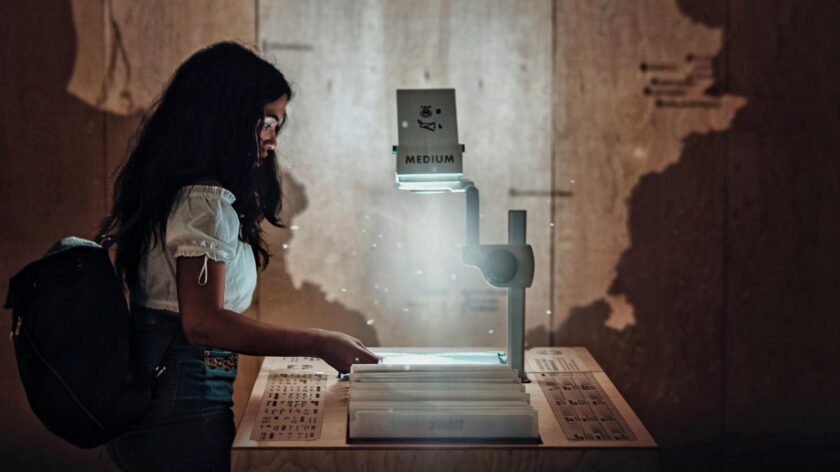 A young woman interacts with an overhead projector in a dimly lit educational setting.