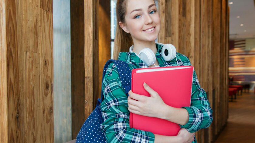 Smiling student holding book and wearing headphones, ready for study.