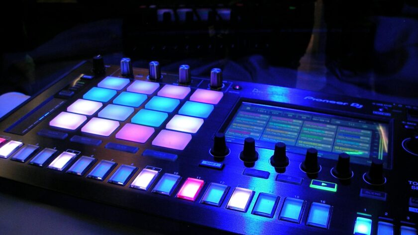 Close-up of an illuminated DJ mixer with vibrant LED pads in a dark studio environment.