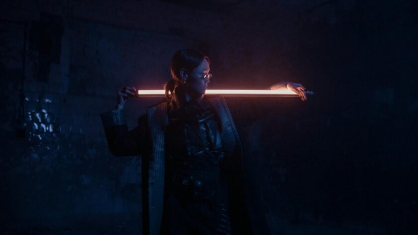 A stylish individual poses with a neon light in a cyberpunk-inspired setting.