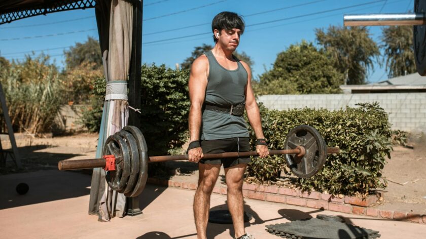 An adult man lifting a barbell outdoors, showcasing strength and fitness.
