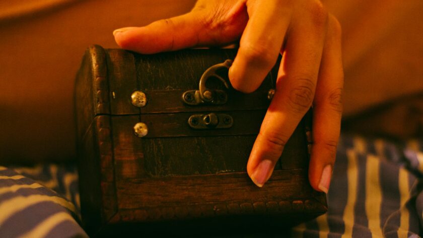 Close-up of a hand holding a vintage wooden box with metal lock, on striped fabric.