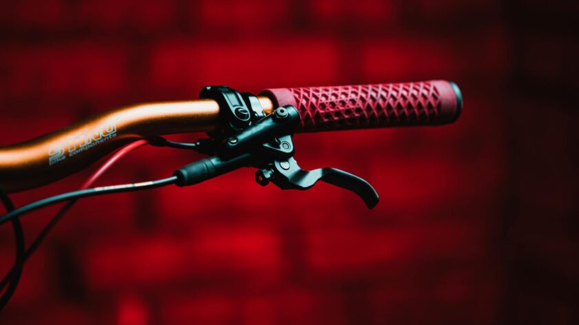 Detailed view of a bicycle handlebar with a red grip. Vivid red backdrop adds contrast.