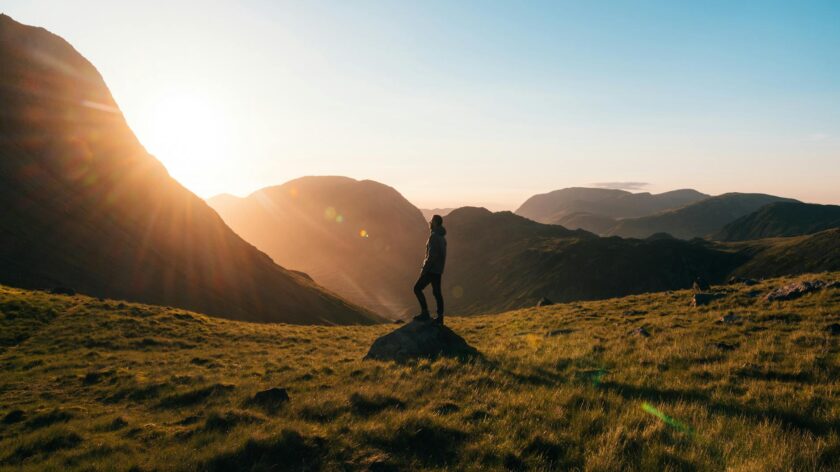 Silhouette of a person standing on a hill during sunrise in Cumbria, England with scenic mountain views.