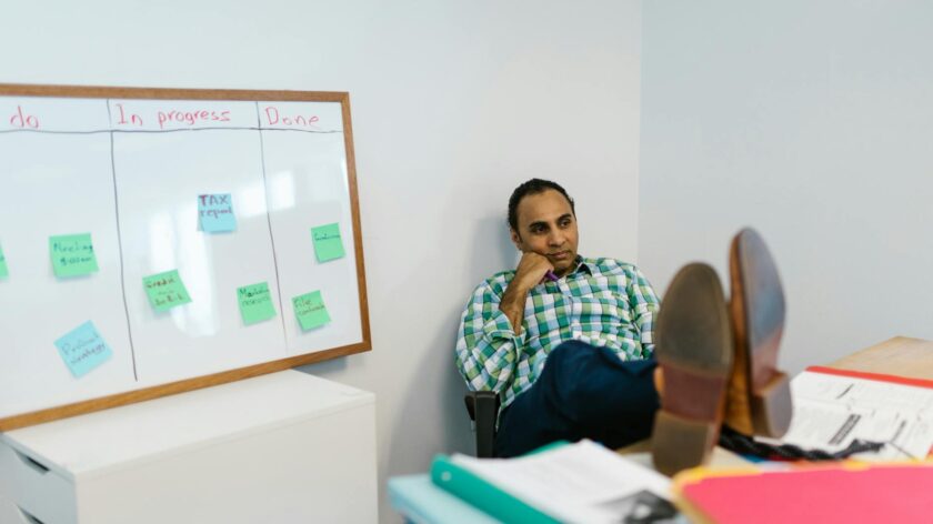 Man in casual attire relaxing at his office desk, contemplating work on a kanban board.