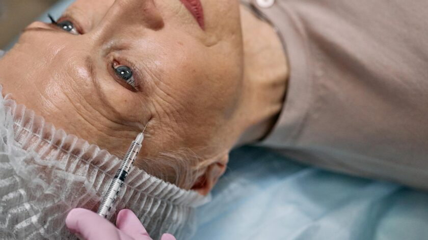 A senior woman undergoes a cosmetic injection procedure in a medical facility.