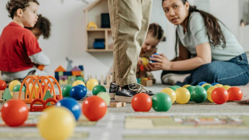 Children and a teacher playing with toys in a kindergarten setting indoors.