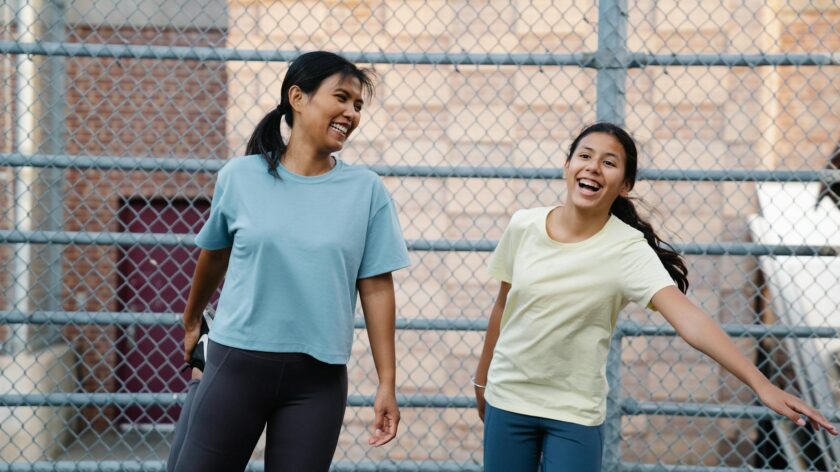 Two women laughing together outdoors, wearing casual T-shirts, joyful moment. Urban setting.