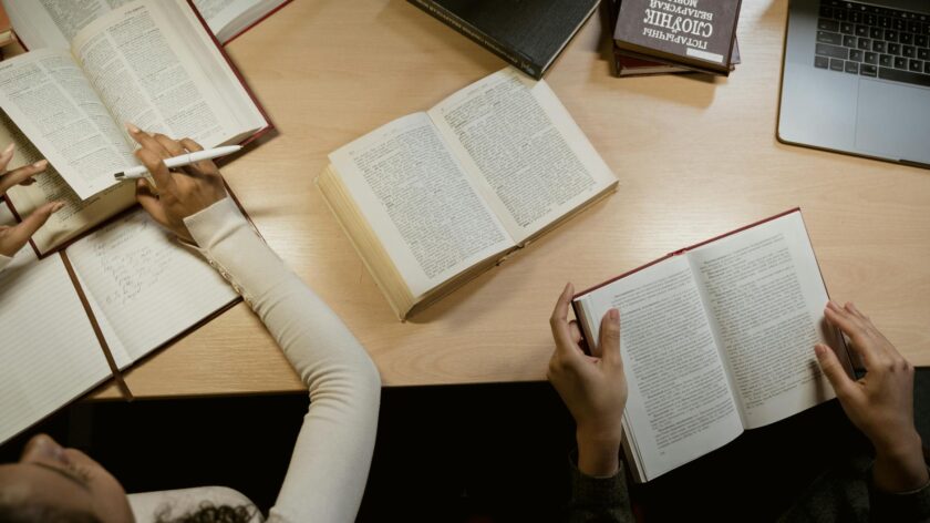 Group of adults studying together with open books and laptops on a wooden table.